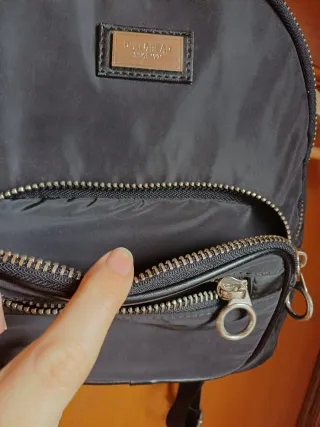 Mochila negra con varios bolsillos. Tiene rozadura