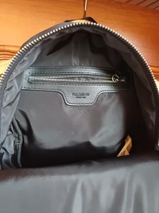 Mochila negra con varios bolsillos. Tiene rozadura