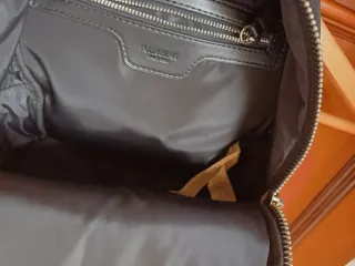 Mochila negra con varios bolsillos. Tiene rozadura
