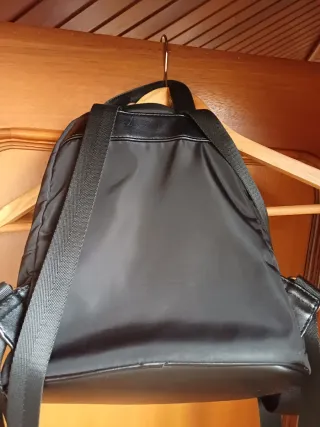 Mochila negra con varios bolsillos. Tiene rozadura