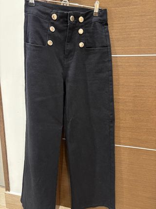 Pantalón negro de tiro alto con botones plateados.
