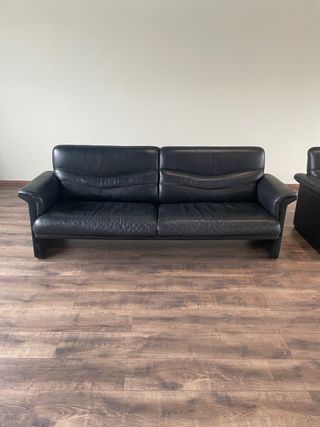 Conjunto de sofá biplaza y sillón de cuero negro.