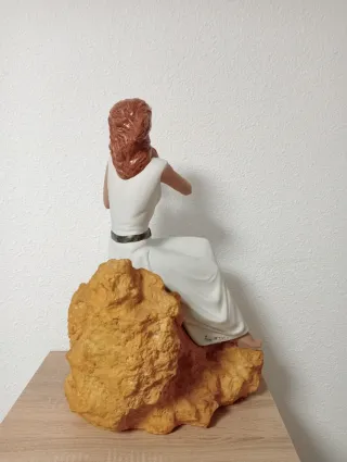 Statuetta natalizia in porcellana di una donna seduta su una pietra