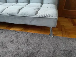 Elegante sofá cama gris con patas decorativas inox