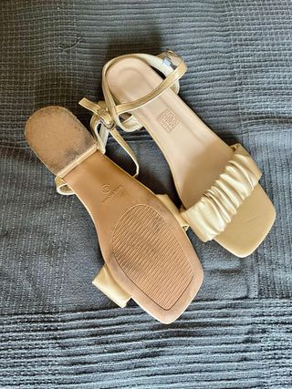 Sandalias doradas planas con tiras fruncidas.