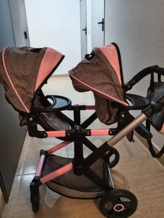 Carro gemelar de juguete gris y rosa.