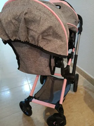 Carro gemelar de juguete gris y rosa.