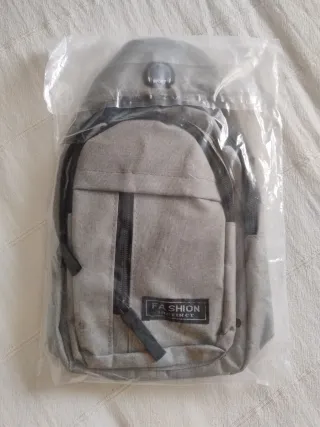 Mochila bandolera pequeña gris, precintada.