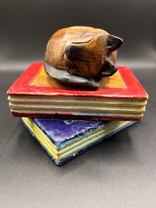 Figura gato de madera sobre libros decorativos