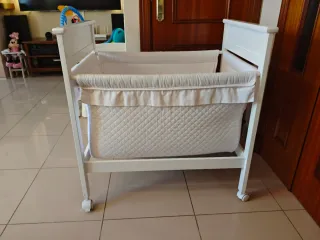 Minicuna blanca de madera con ruedas.