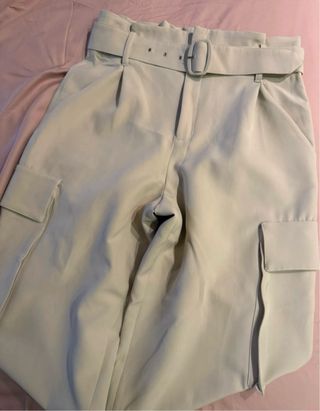 Pantalón de vestir beige con cinturón y bolsillos.