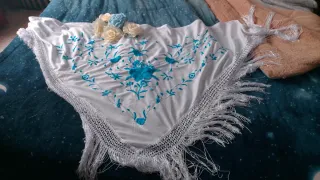 Mantón blanco bordado y flores de adorno.