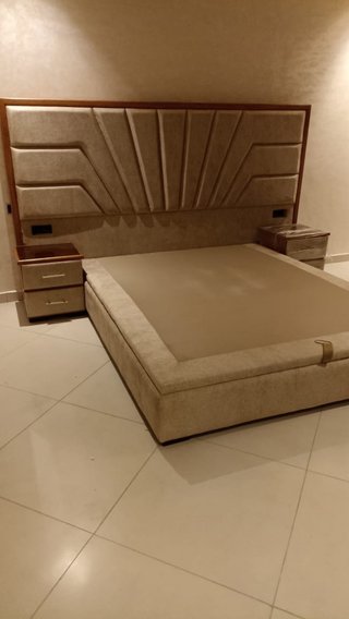 Cama tapizada beige y marrón con mesitas