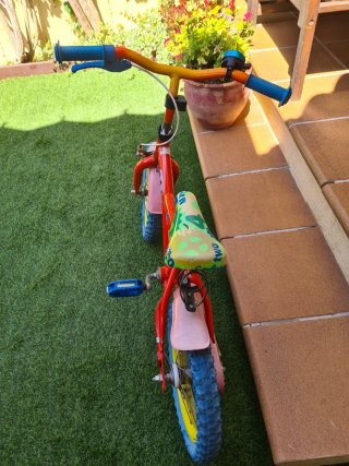 Bici infantil roja con ruedas azules y ruedines