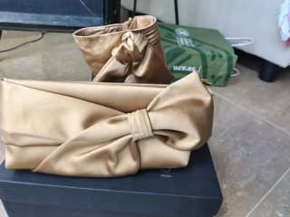 Zapatos de tacón dorados con lazo y bolso a juego.