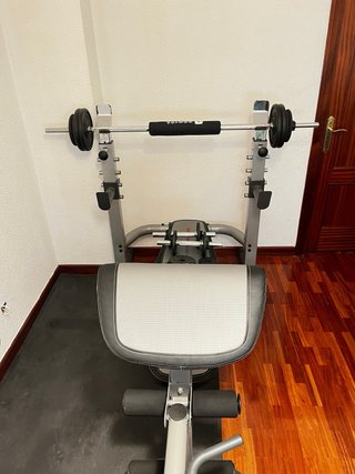 Banco de pesas con barra y mancuernas.