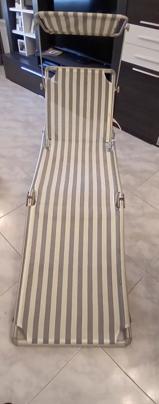 Tumbona plegable gris con bamdas blanco y azul.