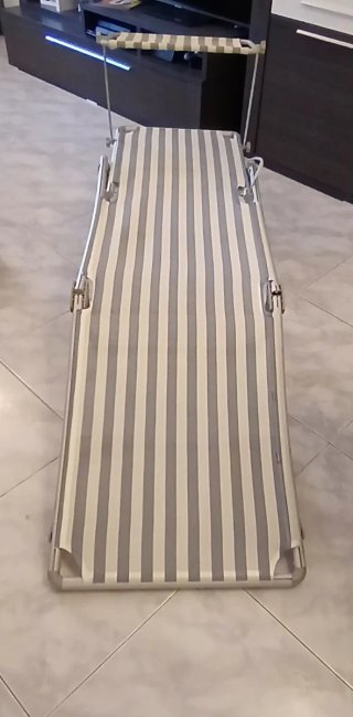 Tumbona plegable gris con bamdas blanco y azul.