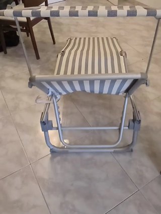 Tumbona plegable gris con bamdas blanco y azul.