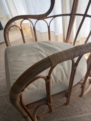 Butaca de mimbre con cojín beige.