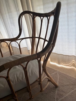 Butaca de mimbre con cojín beige.