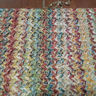 Bolso de mano tejido multicolor con cadena dorada.