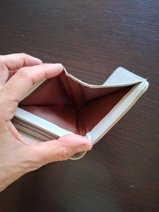 Monedero beige con detalle dorado y borla.