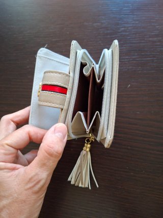 Monedero beige con detalle dorado y borla.