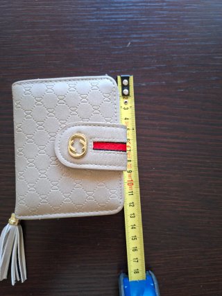Monedero beige con detalle dorado y borla.