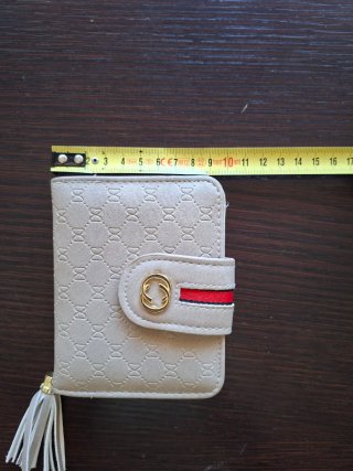 Monedero beige con detalle dorado y borla.