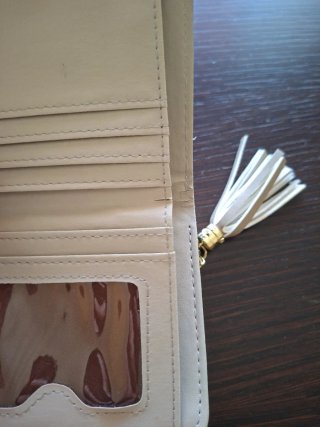 Monedero beige con detalle dorado y borla.