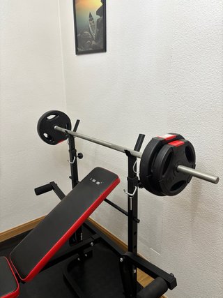 Banco de pesas multifuncional con barra y discos.