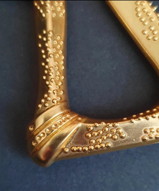 Broche dorado con diseño de sierra antigua.