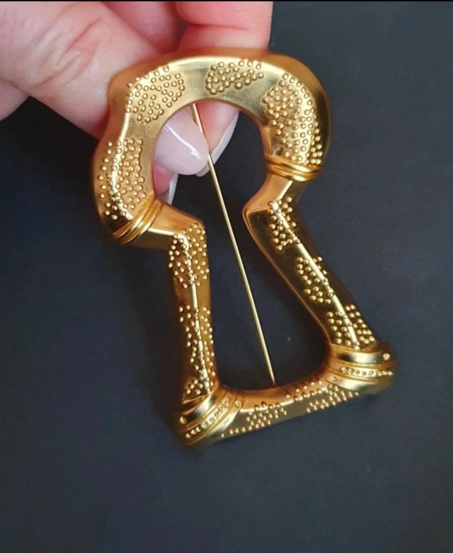 Broche dorado con diseño de sierra antigua.