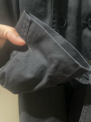 Gabardina negra con cinturón y abertura trasera.