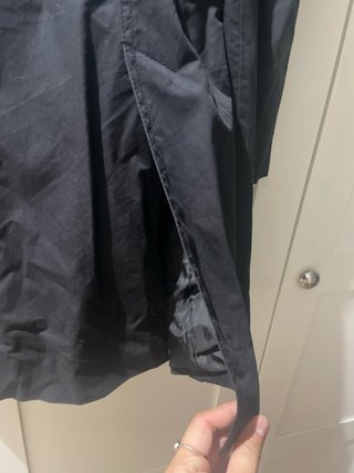 Gabardina negra con cinturón y abertura trasera.