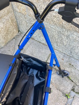 Andador azul con asiento y bolsa. Tiene frenos.