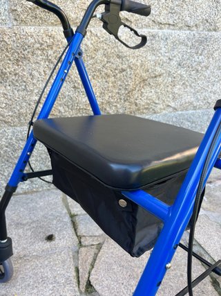 Andador azul con asiento y bolsa. Tiene frenos.