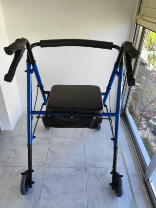 Andador azul con asiento y bolsa. Tiene frenos.