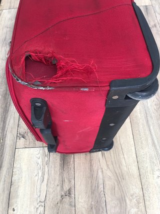 Maleta de viaje roja con ruedas, con daño en tela