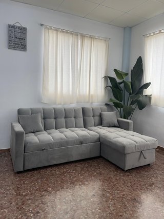 Sofá gris con chaise longue, cama y arcon