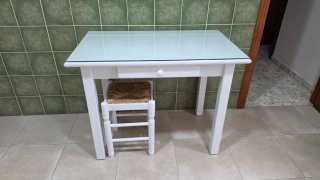 Mesa de madera blanca con cristal, cajón y banco.