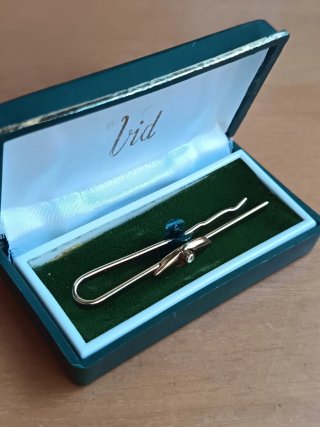 Pasador de corbata dorado con detalle y brillante.