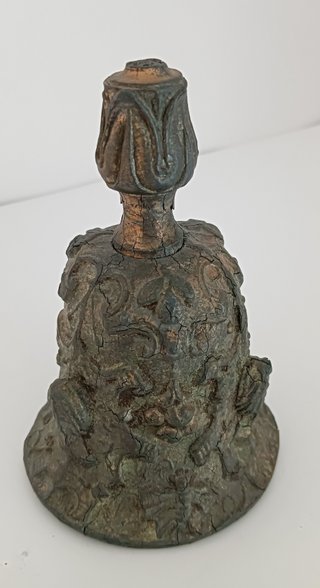 Campana de calamina con relieves de rostros.