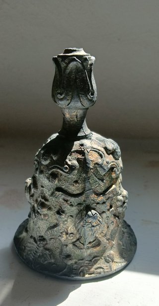 Campana de calamina con relieves de rostros.