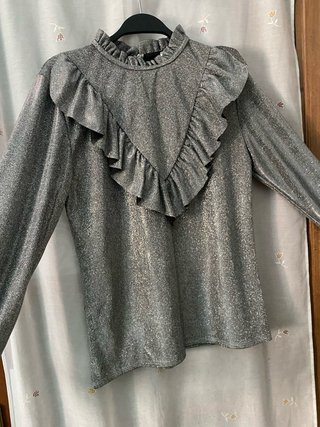 Blusa gris metalizada de manga larga con volantes.
