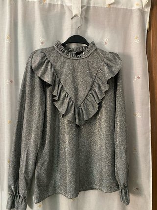 Blusa gris metalizada de manga larga con volantes.