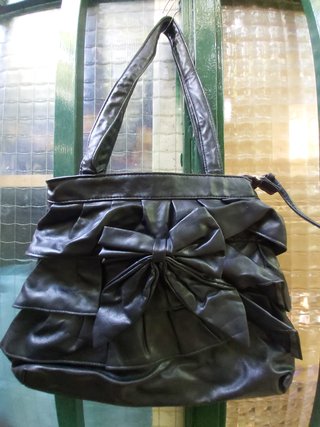 Bolso juvenil negro con adorno de lazo y volantes.