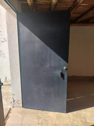 Puerta metálica oscura, sin marco, con cerradura