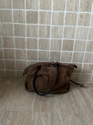 Bolso grande marrón de cuero, con una correa rota.